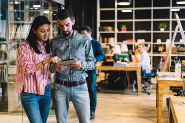 Zeki çoklu etnik kadın ve erkek, ahşap masalar ve öğrencilerle dolu geniş bir kütüphanede kağıt tablet çizmekten bahsediyorlar.