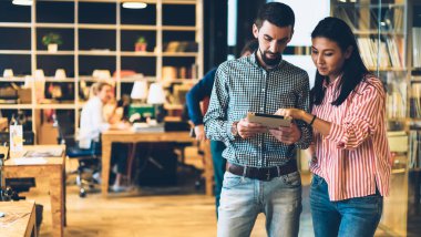 Gülen, çok ırklı kadın ve erkek, ahşap masalar ve öğrencilerle dolu geniş bir kütüphanede kağıt tablet çizmekten bahsediyor.