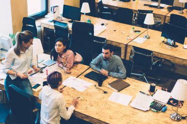 Yukarıdan gelen zeki içerikli çok ırklı öğrencilerin çalışma alanındaki dizüstü bilgisayarlı ve tabletli belgelerle enerjik bir şekilde konuşmaları ve çalışma sürecini tartışmaları