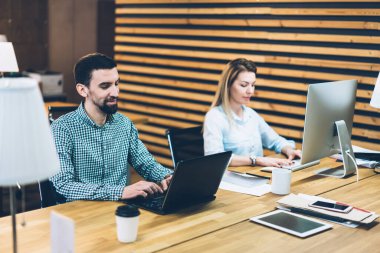 Neşeli çalışkan erkek ve kadın, odasındaki ahşap masada dizüstü bilgisayara ve modern bilgisayara yoğunlaşmışlar.