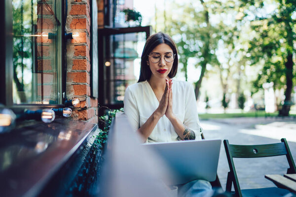 Skilled woman in classic glasses waiting for email confirmation about online web order via laptop computer, attractive woman checking blog statistic during leisure time in coworking street terrace