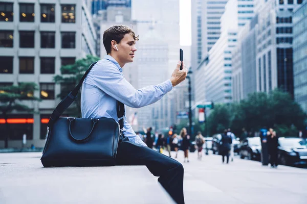 Side view of executive male person communicating with service operator for online consultancy about 4g roaming internet for business trip, young proud ceo in earbuds using bluetooth for calling