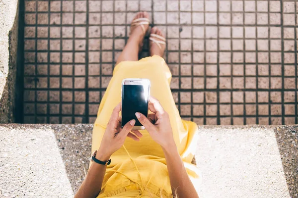 在阳光明媚的夏日 坐在街上的石凳上 穿着鲜艳的黄色连衣裙 头戴金色鞋子 头戴智能手机的无脸女士 — 图库照片