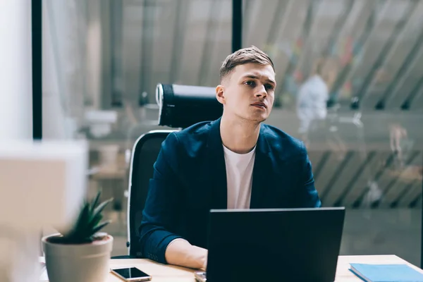 Puzzled interested focused specialist looking away during occupation on startup project on laptop at table and listening to noise outside office