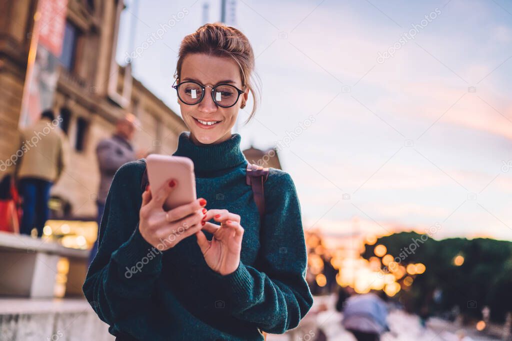 Cheerful hipster girl in classic eyeglasses for provide eyes protection enjoying communication during free time for exploring historic city, happy woman searching funny comments near publication