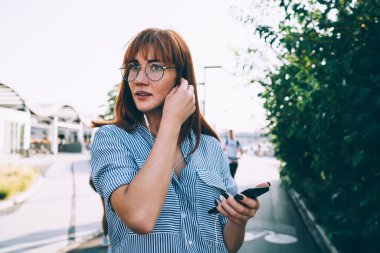 Gözlüklü çekici bir kızıl kadın kulaklık takıyor. Cep telefonuyla müzik listesi dinliyor. Hippi kız Melloman akıllı telefon ve elektronik aksesuarla internet radyosundan keyif alıyor.