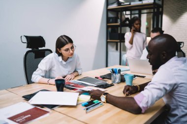 Erkek işçi, öğleden sonra ofisteki cep telefonuyla konuşurken kadın meslektaşına belge gösteriyor ve fikirlerini dile getiriyor.