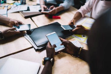 Yukarıdan tanınmayan çok ırklı girişim grubunun iş yerinde proje üzerinde çalışırken modern cep telefonlarıyla sohbet etmesi