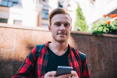 Kırmızı-siyah tişörtlü ve siyah tişörtlü mutlu bir erkek yazın şehirde gezintiye çıkıyor.