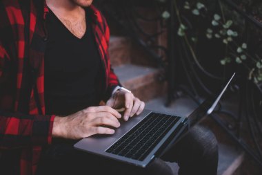 Ev merdivenlerinde yeni bir proje oluşturmak için dizüstü bilgisayar kullanarak günlük giyim kontrol ağı kullanan genç adamın kırpma görünümü