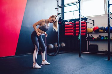 Spor kıyafetleri içinde çekici bir kadın. Vücut üzerinde çalışıyor. Süspansiyon bantları kullanıyor.