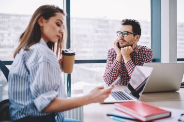 Modern ofisteki genç bayan iş arkadaşıyla çalışırken şık giyinen düşünceli bir erkek ofis çalışanı akıllı telefondan arıyor. 