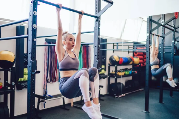 体育服中的女性 身材匀称 双腿凸起 做运动 呼吸挂在水平杠上 锻炼腹部肌肉 — 图库照片