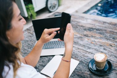 Bilgisayarlı ve kahveli masada otururken boş akıllı telefondan mesaj atan ve rahat bir kafede defter açan bir kadın.