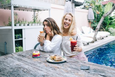 Rahatlamış gülen arkadaşlar kameraya sarılıyor, yüzünü ekşitiyor kokteyller ve jöleli tatlılar ile masada oturuyor mavi kristal yüzme havuzlu. 