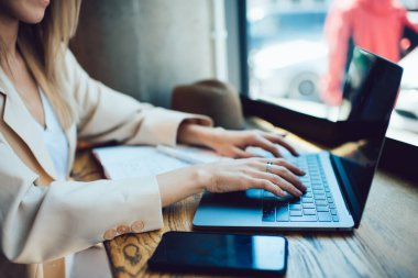 Modern şehir kafesinde masa başında uzaktan çalışırken bej rengi gayri resmi takım elbiseli kadın klavyede daktilo kullanıyor.