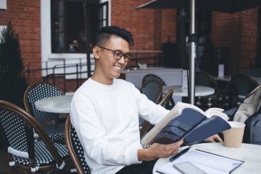 Entellektüel Asyalı neşeli, gözlüklü, ders kitabı okuyan, sokak yemekhanesinde edebiyat ödevi yapan modern bir adam.