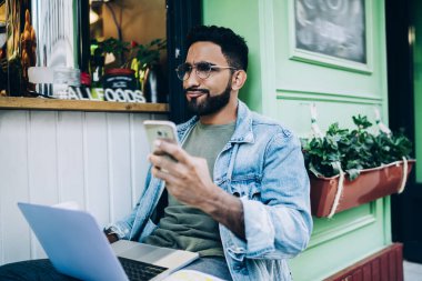 Hüsrana uğramış modern adam elinde cep telefonu tutan ve haberlerden memnun kalmayan kafenin yanındaki bankta dizüstü bilgisayarla oturan