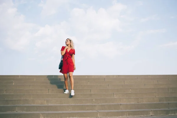 空を背景に眺めながら大きな石段の上に立つ短い赤いドレスの若い公正な髪の女性 — ストック写真