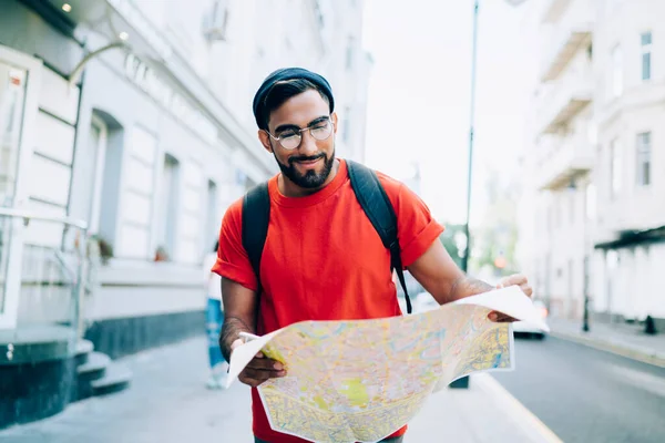 穿着黑色帽子橙色T恤 背着背包看地图站在大城市街道上的男性微笑 — 图库照片
