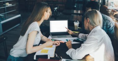 Meslektaşlarıyla çalışırken beyaz boş dizüstü bilgisayara bakan ve kafede iş fikirlerini tartışan bir kadının yan görüntüsü
