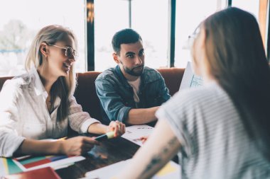 Gündelik giysiler içindeki genç ve başarılı meslektaşlar kafeteryada birlikte otururken projeyle ilgili görüşlerini paylaşıyorlar.