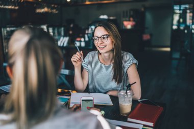 Zeki, gülümseyen entellektüel meslektaşlar. İçi dokümanlarla dolu bir masada oturuyorlar. Yaratıcı iş yerinde renkli kahve etiketleri.