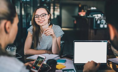 Zeki entellektüel iş arkadaşları cep telefonlarında sörf yaparken dizüstü bilgisayarlarını izliyorlar. Yaratıcı iş yerlerindeki renkli çıkartmalarla dolu masada oturuyorlar.
