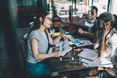 Grafikleri olan, gülümseyen ve iş arkadaşının kafenin penceresinin arkasındaki serbest iş arasında komik bir hikaye anlattığı kadınların yan görüntüsü.