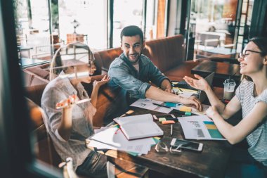 Neşeli genç adam gülümseyip sohbet ediyor ve pencerenin arkasında oturmuş restoranda uzaktan kumandayla dinlenirken kadın meslektaşlarına el sallıyor.