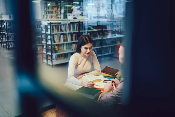 大学図書館のテーブルに座っている間に男性の友人と宿題をする本や文房具で若い女性を笑顔 — ストック写真