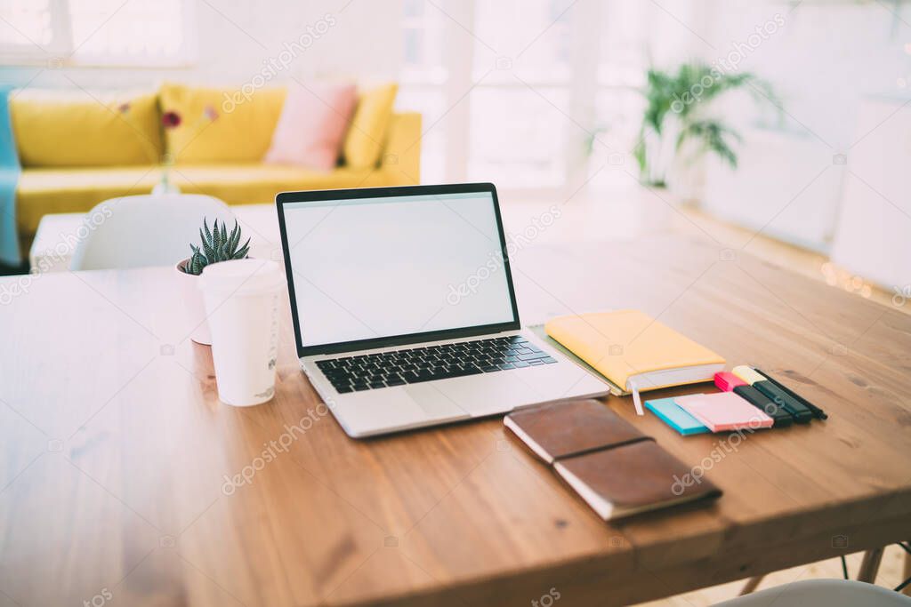 Workspace consisting of opened laptop with blank screen and office supplies with notebooks on wooden table with coffee on blurred background