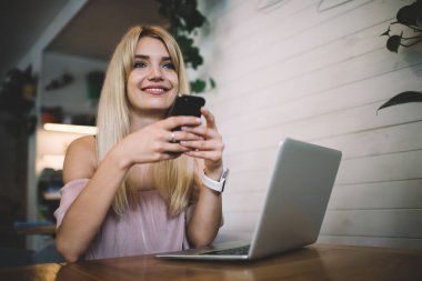Genç başarılı bayan serbest çalışan müşteriye cep telefonuyla mesaj gönderiyor. Laptopla masada oturuyor ve kafede proje üzerinde çalışıyor. 