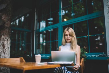 Kolsuz gömlekli, sarışın, laptopla çalışan, şehirde bir kafede laptoplu ve kahveli bir kadın.