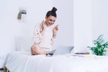 Genç, neşeli kız öğrenci bacak bacak üstüne atmış ve parmaklarını çapraz tutarak sınava giriyor. Laptopla sonuçlanıyor ve yatak odasında gülümsüyor. 