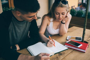Fotokopi defterine yazı yazan zeki bir kız öğrenci ve grup arkadaşına çözümü anlatırken aynı anda kafe terasında buluşup ödev yapıyorlar.