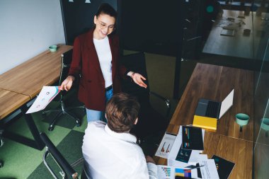 Yukarıdan bakıldığında, gözlüklü neşeli bayan ofis çalışanı, bilgisayarın yanında boş bir ekranla dururken tanınmayan bir iş arkadaşıyla konuşuyor.