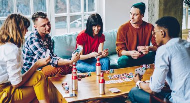 Masanın etrafında poker oynarken ve evde birlikte harika vakit geçirirken içki içerken çok ırklı, yoğun bir takım elinde kart tutuyor.