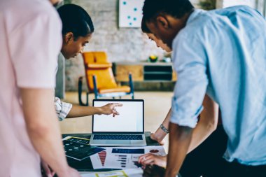 Modern ofisteki boş ekran dizüstü bilgisayarda birbirlerine destek veren çok ırklı uzmanların arka plan görüşü