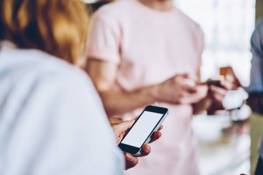 Yüzsüz kadın boş ekrana odaklanıyor ve aydınlık modern ofisteki iş arkadaşlarıyla iş görüşmeleri sırasında akıllı telefon kullanıyor.