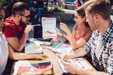 Yazın açık terasta doküman grafikleri ve çizelgelerle konuşan ve masada oturan serbest çalışanlardan oluşan bir grup. 
