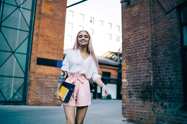 細い笑顔女性で白いシャツとピンクのショートパンツともに長いですピンクの髪歩く通りを保持本とフォルダで手 — ストック写真