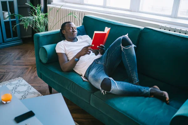 Cima Jovem Afro Americano Jeans Rasgado Deitado Sofá Descansando Lendo — Fotografia de Stock