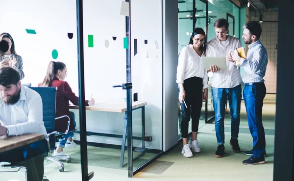 Jolly and glad office employees in neat shirts standing in bright corridor and laughing while watching videos in social media