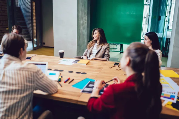 近代的なオフィス空間でテーブルの周りで仕事をしながら戦略を立案し お互いを見ている若いフレンドリーなビジネスグループ — ストック写真