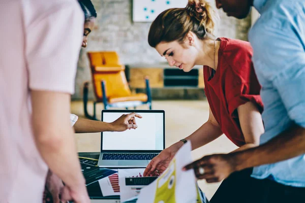 Gündelik kırmızı tişörtlü genç bayan yöneticinin yandan görünüşü belgeyle çalışırken meçhul meslektaşlar modern ofisteki boş ekran laptopuyla çalışıyor.