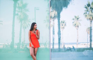 Sıradan kıyafetler giymiş düşünceli hippi turist şehir merkezinde duvarın yanında duruyor cep telefonu cihazıyla internete bağlanıyor, elinde cep telefonu tutan çekici bir kadın.