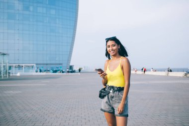 Şehrin boş zamanlarında sosyal medyada gezinmek için cep telefonu kullanan mutlu İspanyol seyahat blogcusunun yarım boy portresi. Cep telefonu teknolojisi olan neşeli hippi kız.