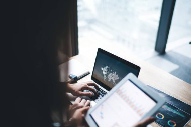 Yukarıdaki kadın verileri gösteren tabletten masadaki yüzü belirsiz patrona bilgisayarla ofisteki dünya haritasını araştırıyor.