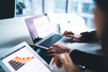 Çalışma masasında oturan ve ofiste dizüstü bilgisayar ve tablet ekranlarında grafikler ve grafiklerle çalışan çalışanlar